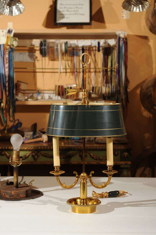 The two scrolling candle lights; joined to a center staff above a dished circular base; all beneath an adjustable oval dark green tole shade with scrolling bipod; the whole surmounted by a ring finial and embellished with an arrow. Very good