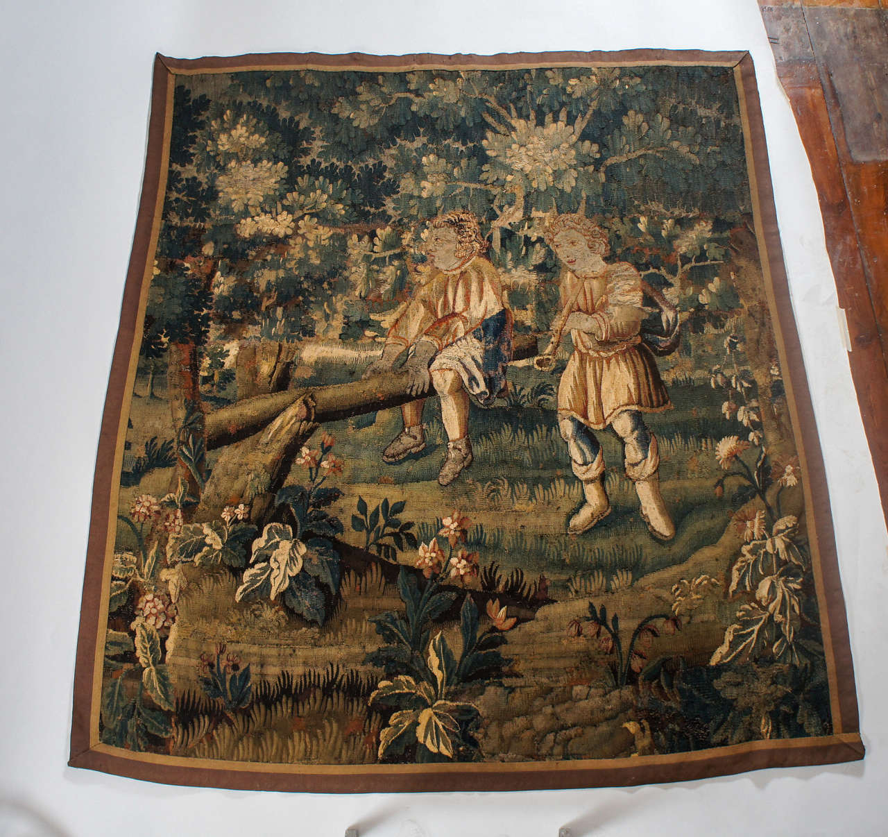 Wonderful first half 17th century Flemish verdure tapestry of two young boys playing in a woodland setting; one sitting astride a fallen tree and the other with musical instrument.  Exquisite coloring; wonderful piece.