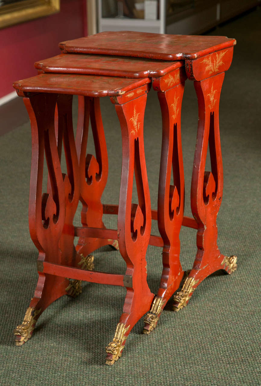 A set of three red chinoiserie nesting tables with raised gilt decoration and dragon feet.
