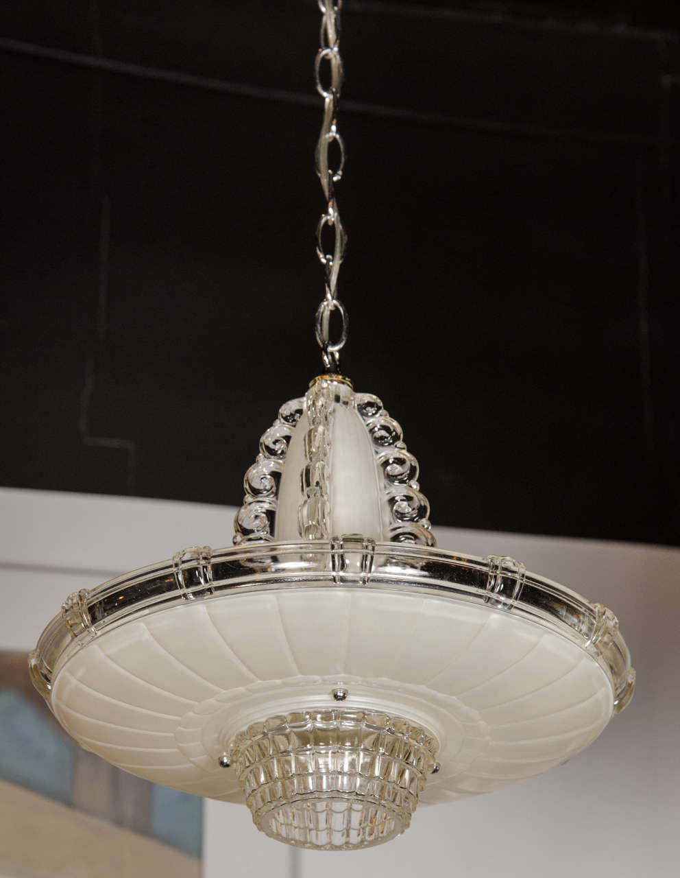 This elegant Art Deco chandelier by Lightolier features a fountain-like form, thick art glass with geometric designs and textures throughout the different sections. It has alternating frosted and clear colored glass which emanate a warm glow when
