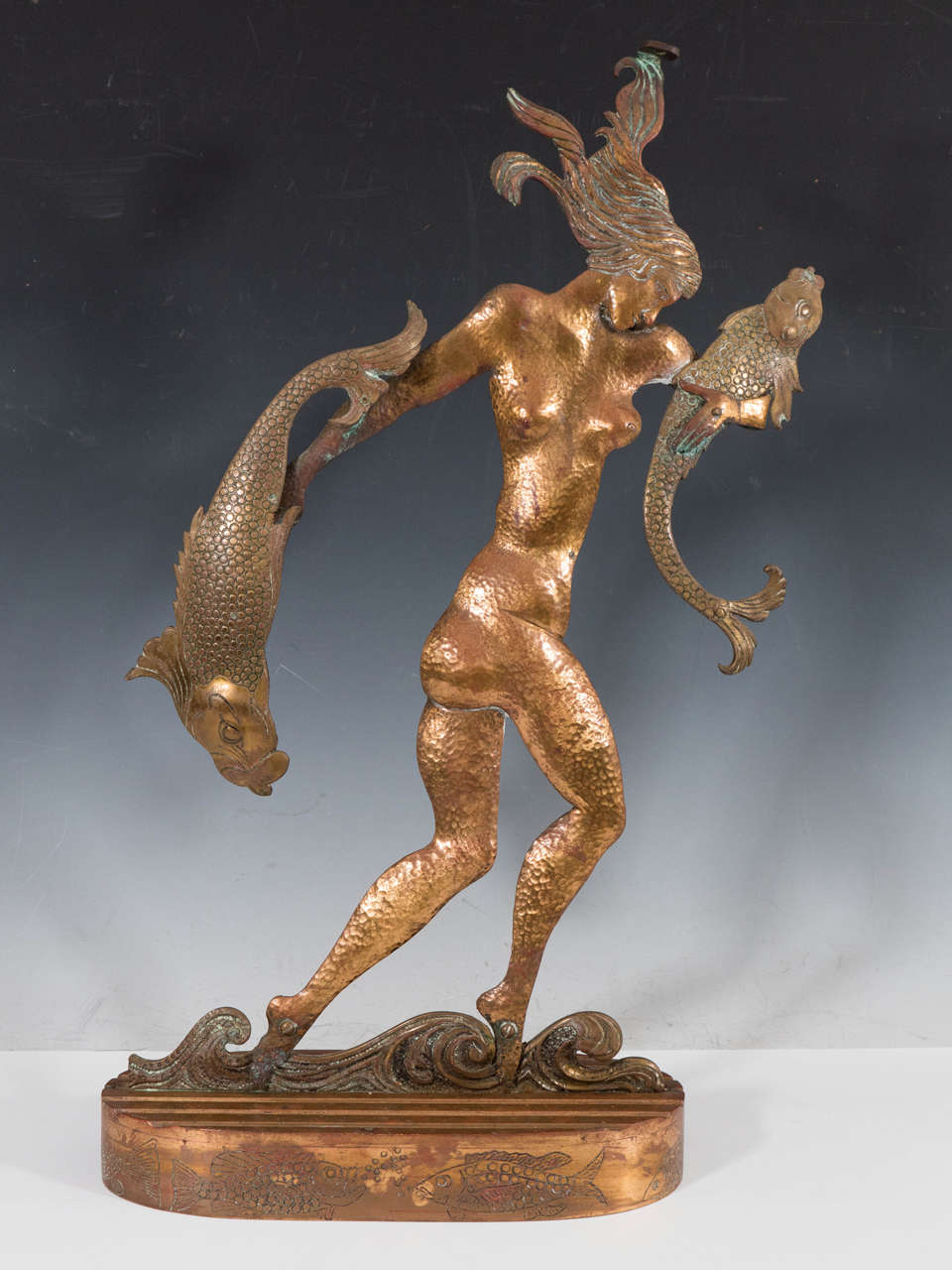 An Art Deco hammered copper sculpture of a nude woman wading through water and carrying two fish in the style of Hagenauer.