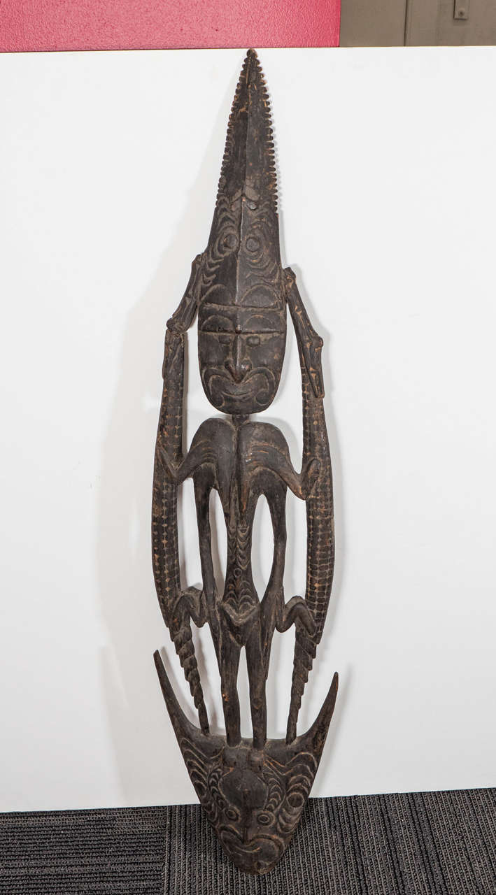 A vintage Papua New Guinea wooden suspension hook ('Samban' or 'Tshambwan') from the Iatmul People of the Sepik River region, carved on both sides, featuring a stylized figure, flanked by two crocodiles. This wooden hook possesses both utilitarian