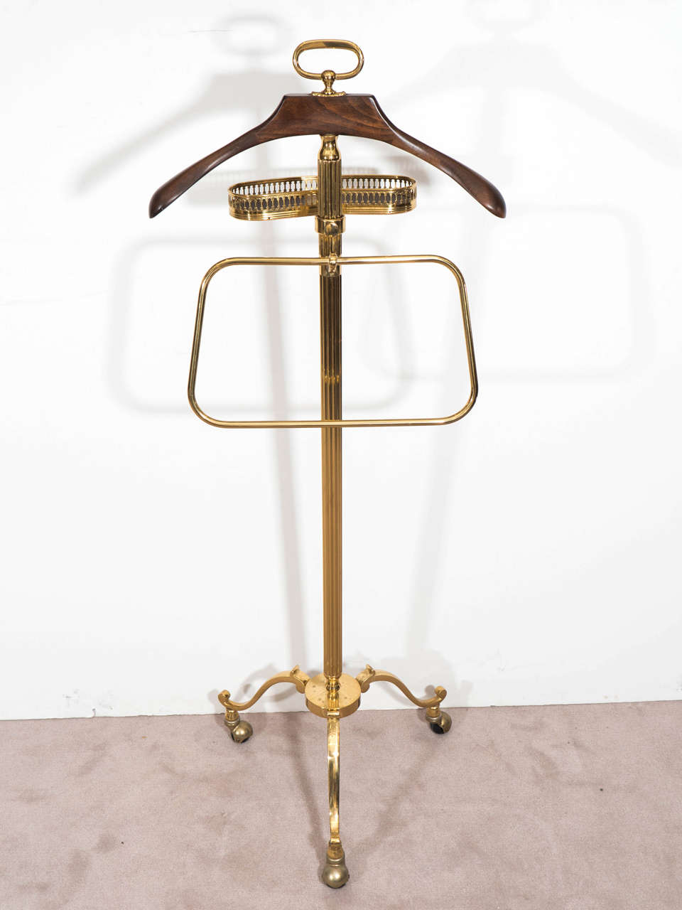 A midcentury circa 1960s Italian solid brass valet, with adjustable coin or jewelry holder with leather insert, and wooden hanger, affixed to round reeded pole on tripod base with casters. Good vintage condition with age appropriate wear.