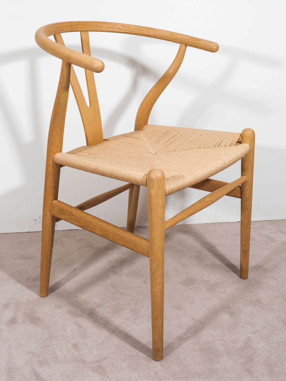 A contemporary pair of wishbone arm chairs in wood with back-splat and paper-cord seats. A sticker on the bottom of each denotes design by architect Hans J. Wegner, for Carl Hanson & Co and production date 2006. Good condition with some bleaching