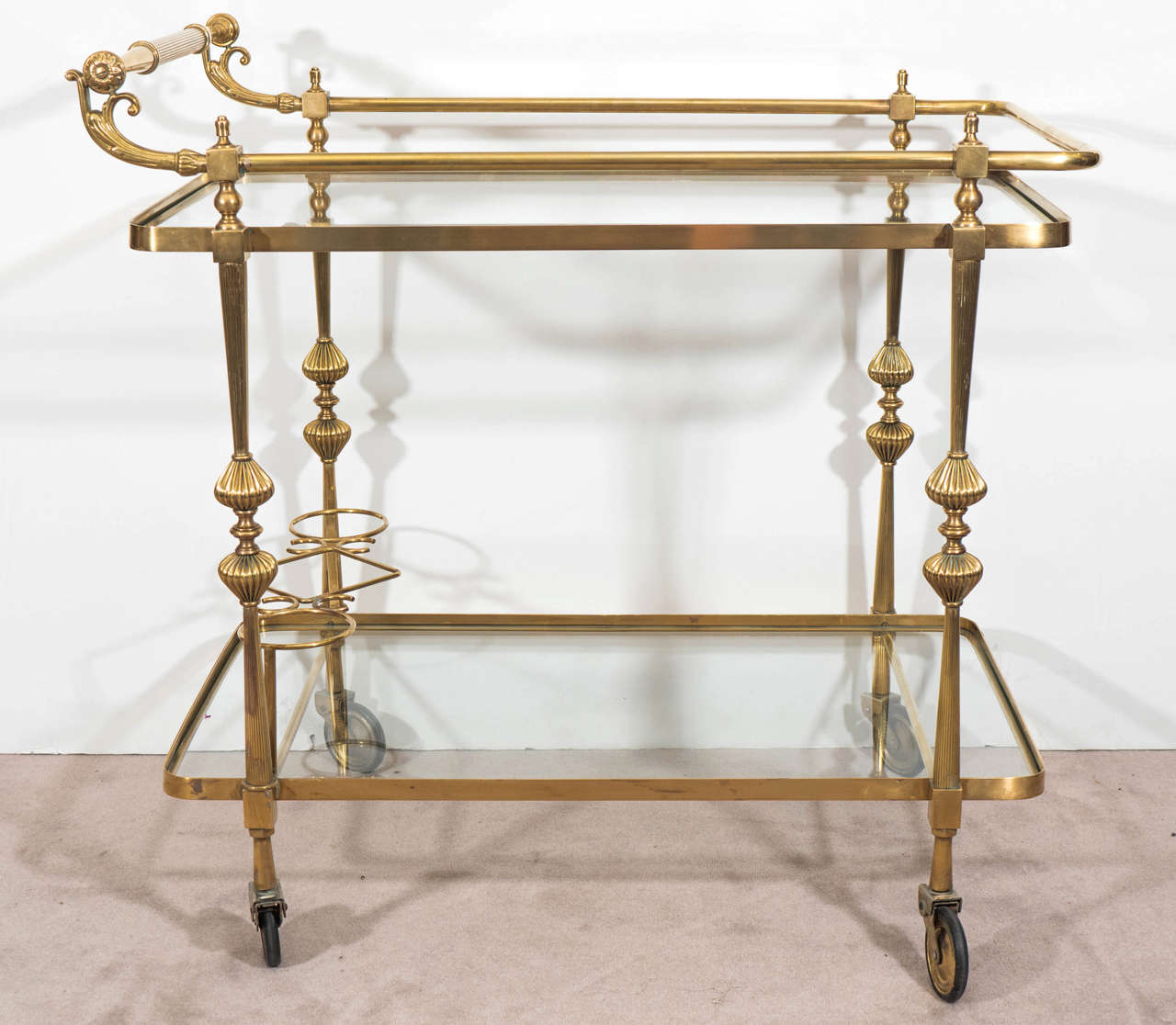 A vintage Hollywood Regency Italian two-tier brass bar cart, manufactured circa 1950's, inset with glass shelves on reeded, round tapering legs with wine holders. Good vintage condition with age appropriate wear and newly replaced glass.