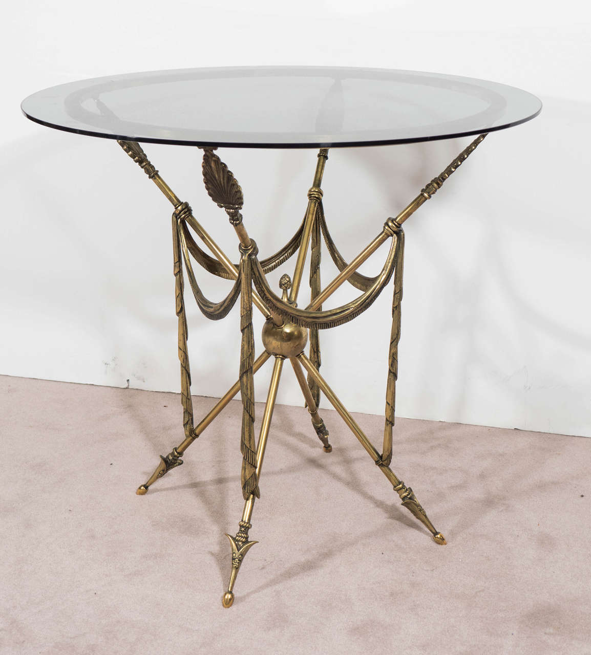 A vintage pair of French brass end or side tables, with arrow motif and neoclassical elements, circa 1950s. Smoked glass tops above a brass ring base, supported by four crossed legs, each stylized with anthemion vanes, terminating into decorative