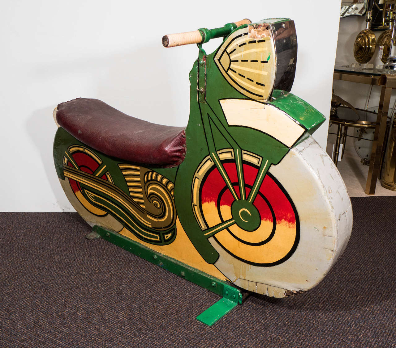 A 1930s wooden motorcycle sculpture for an amusement park, hand-painted with leather seat, standing on original, enameled green iron base. Chrome accent at headlight, great colors and graphics. May have been used for children's ride or carnival