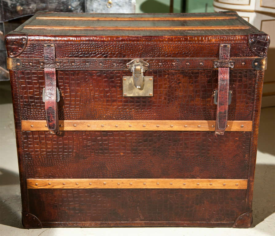 A decorative English faux alligator-skin leather trunk, two leather straps with a patinated silver lock, opens to a storage.