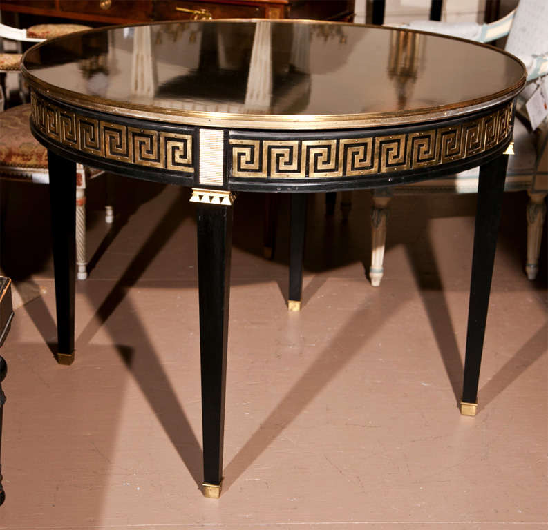 A glamorous French neoclassical style center table, circa 1940, overall ebonized, the circular top with bronze banding atop a frieze decorated with parcel-gilt Greek-key pattern, raised on four squared tapering legs ending in capped feet. By Maison