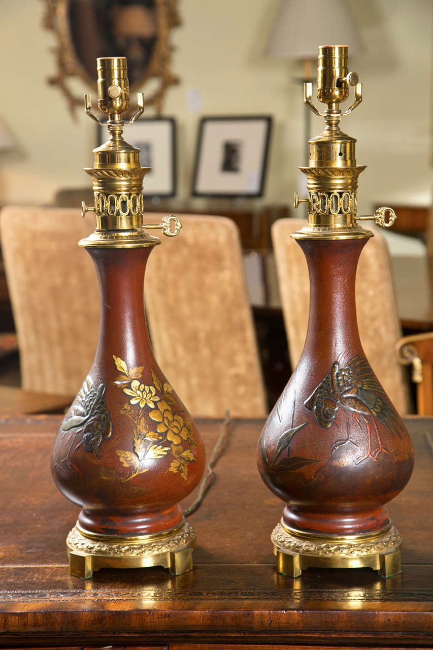 A pair of French parafin lamps decorated in red lacquer with raised gilt birds.