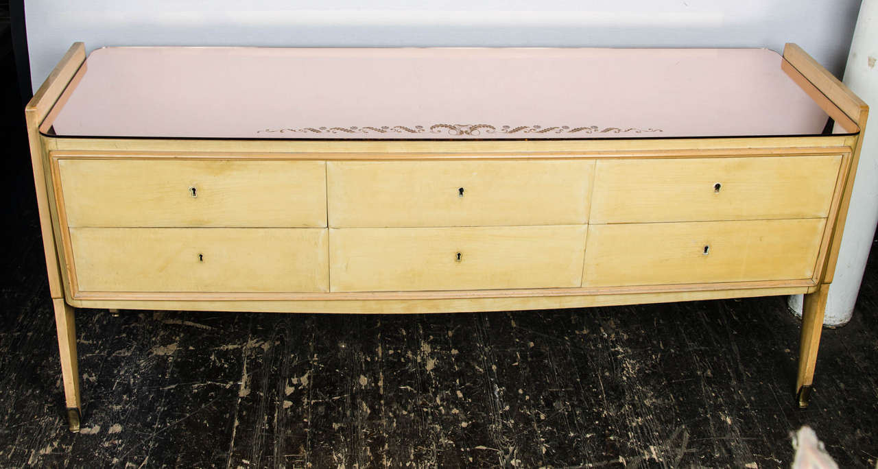 1950s chest of drawers in parchment and ash with a pink glass top and decorative brass feet endings.
