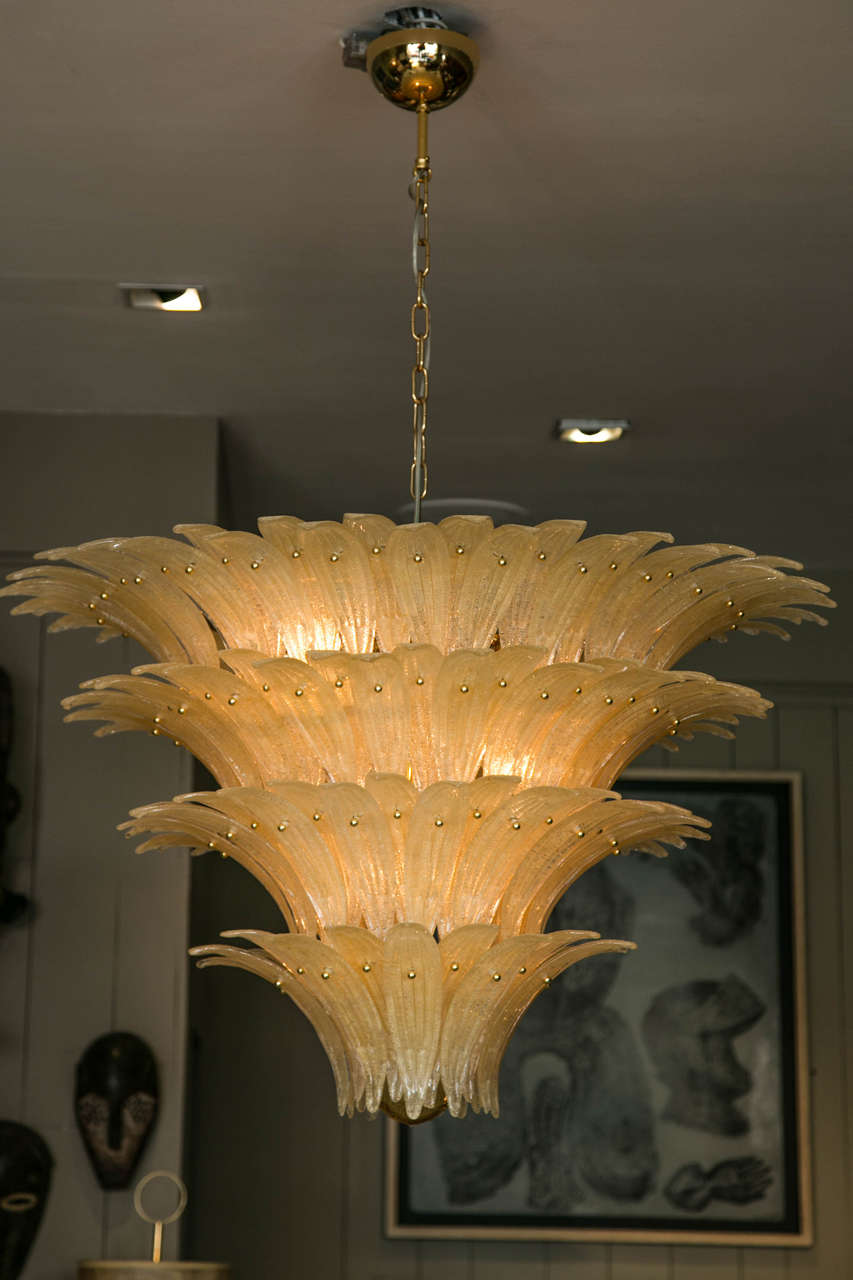 Murano glass chandelier composed of four-tiers of handblown, palm leaves attached to a gilded structure, with a glass ball finial. 
The palm leaves are gold color curved glass with a sand finish on one side which gives a nice warm color to the