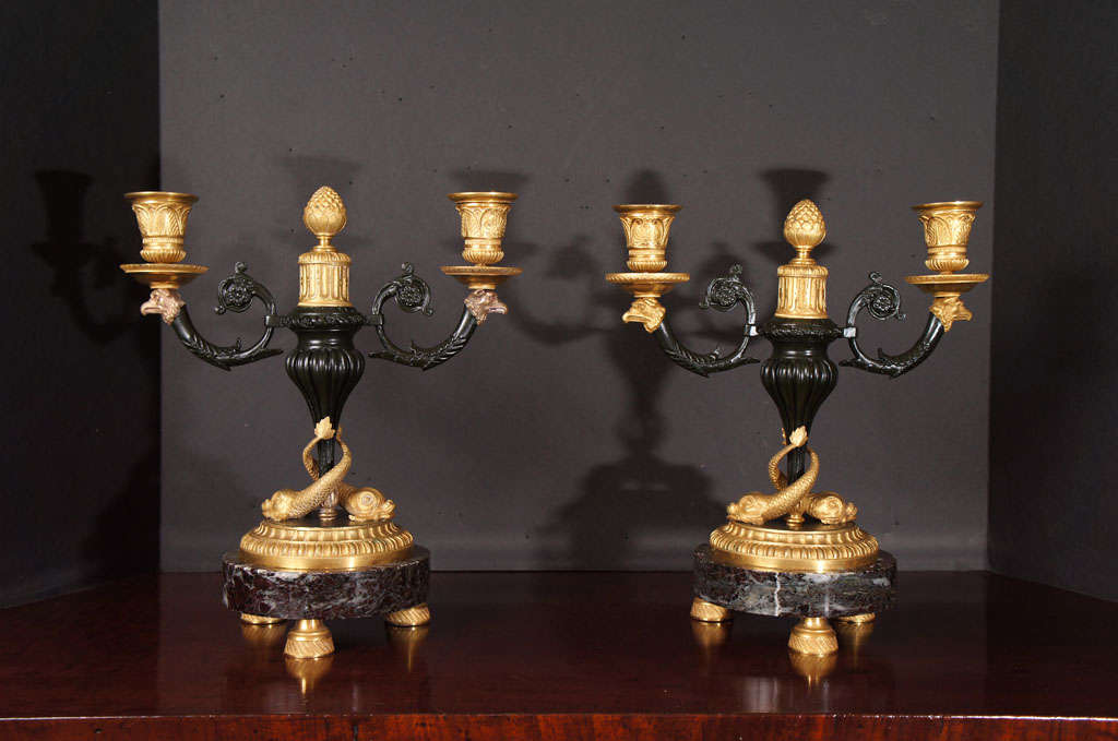 Este par de candelabros de dos luces están finamente fundidos, con gran detalle y un fino cincelado a mano. El trabajo en bronce se realiza tanto en dorado mate y bruñido como en patinado, lo que hace que el trabajo sea largo y laborioso, creando un