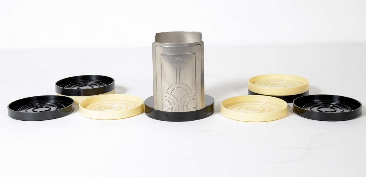 This set features a set of 8 bakelite coasters in alternating creme and black fitted in a very stylized Art Deco geometric design holder in polished aluminum.It really epitomized the Machine Ages influence on Art Deco in America.