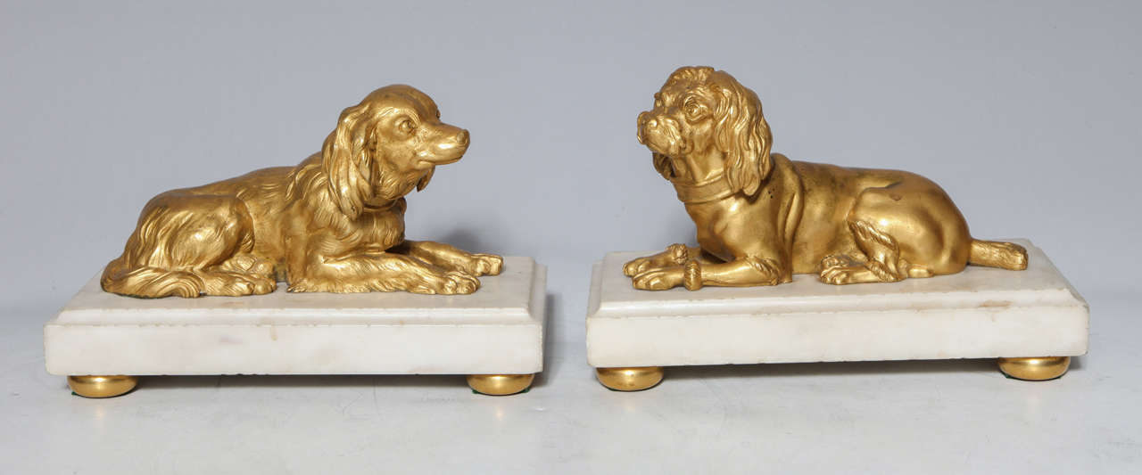A rare pair of French Louis XVI doré bronze dogs recumbent on Carrara marble bases with bronze circular feet. Each dog has individuated features imbuing the dogs with a lifelike, unique air, Paris, circa 1810.