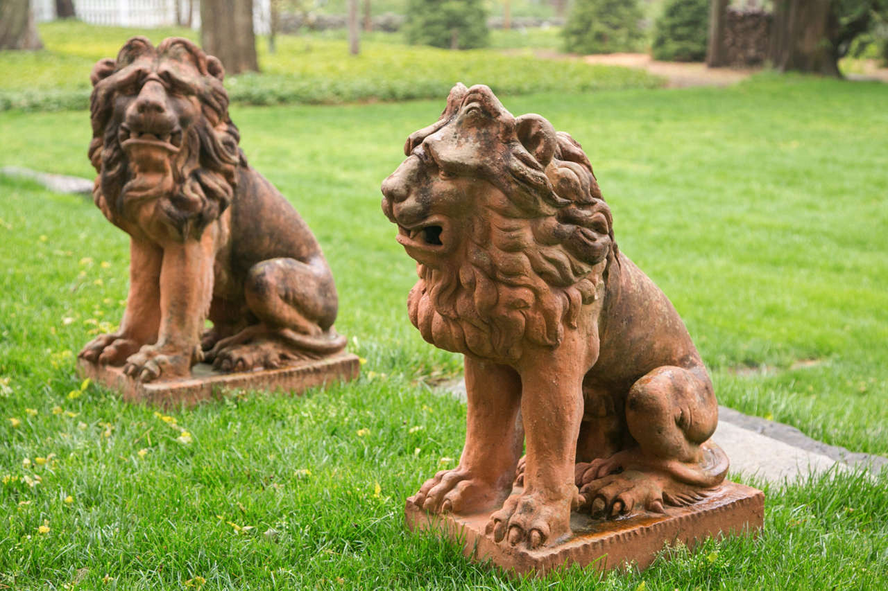 A pair of 17th century style terra cotta lions seated on their haunches with animated expressions, their fully-maned heads turned in opposing directions.
