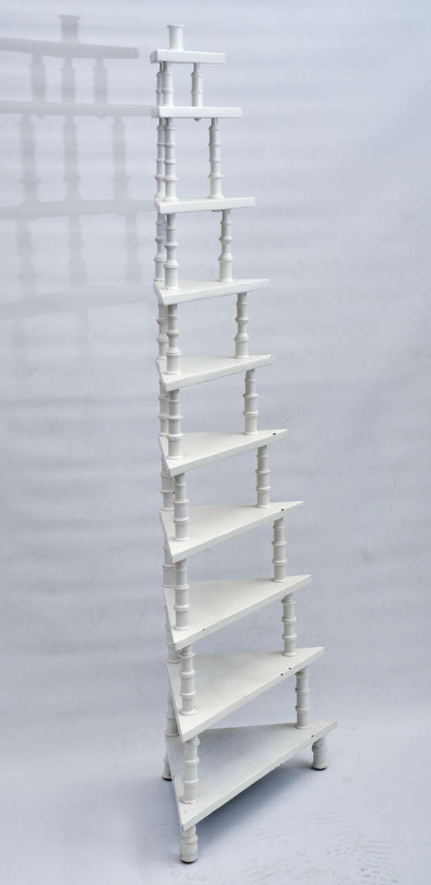 A vintage white painted wood corner shelf with ten levels constructed of thread spools.