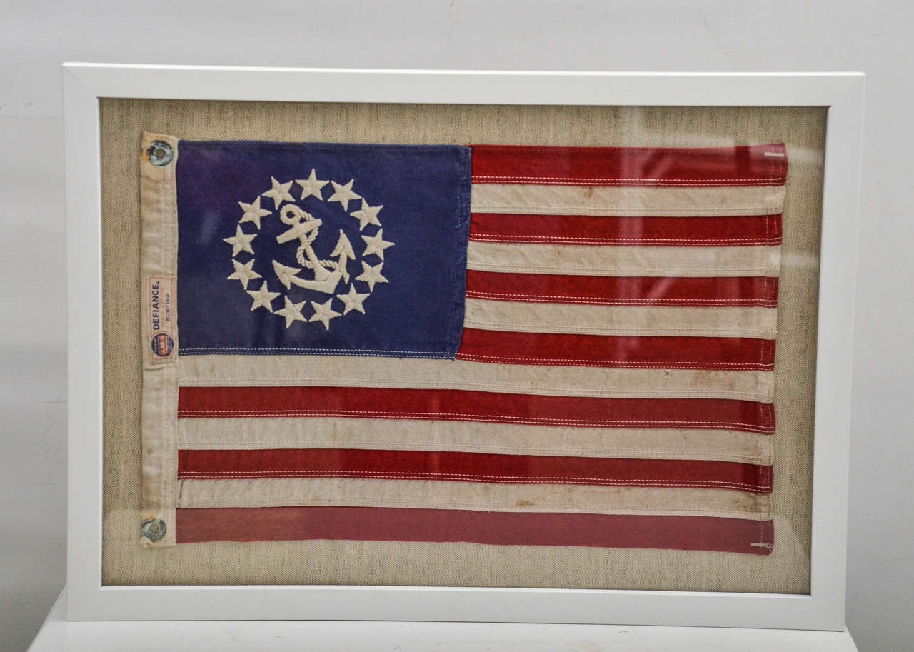 A vintage thirteen star US Yacht Ensign flag mounted on burlap matte and framed in white.