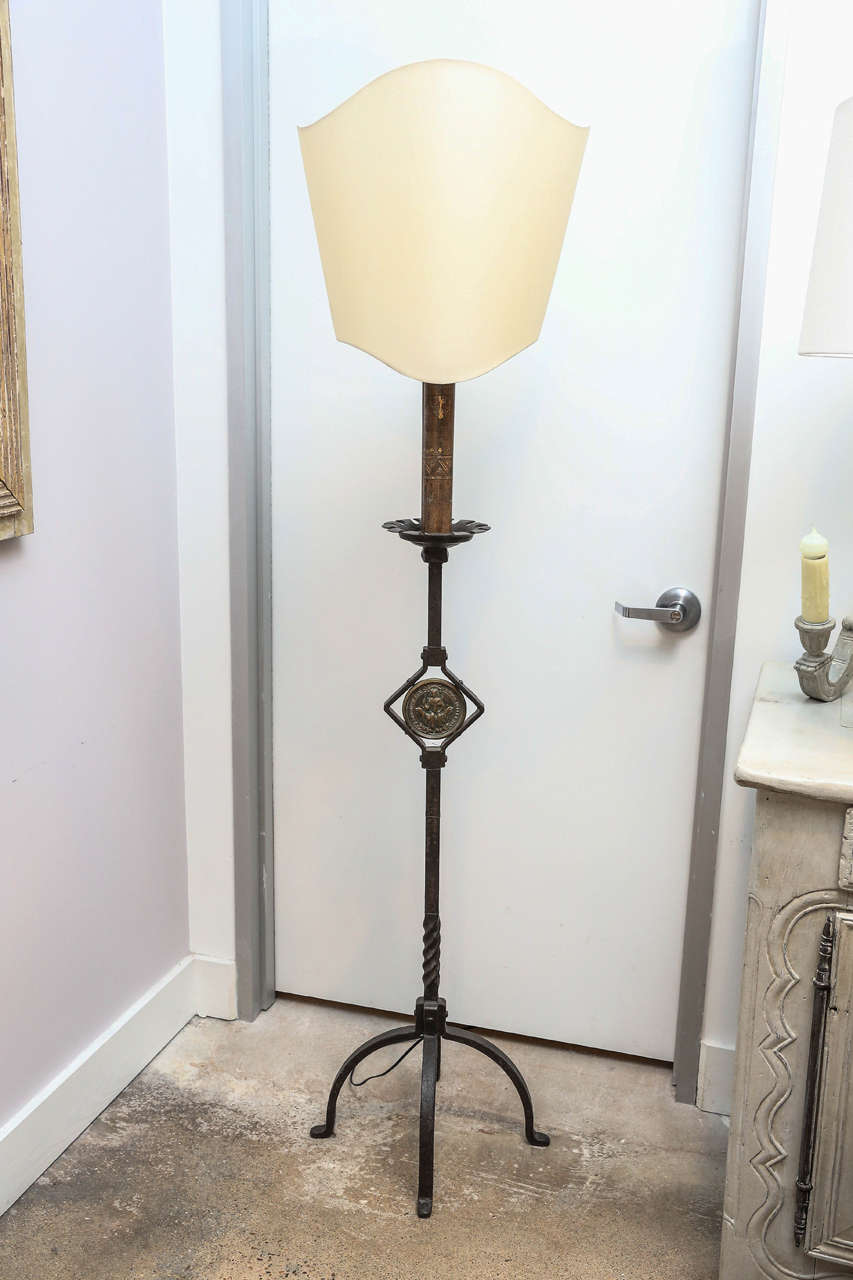 19th century heavy for forge French candle stand with earlier cast bronze medallion insert and hand-painted antique tin candle sleeve, wired as custom floor lamp with vintage shield-shaped rolled-edge shade.