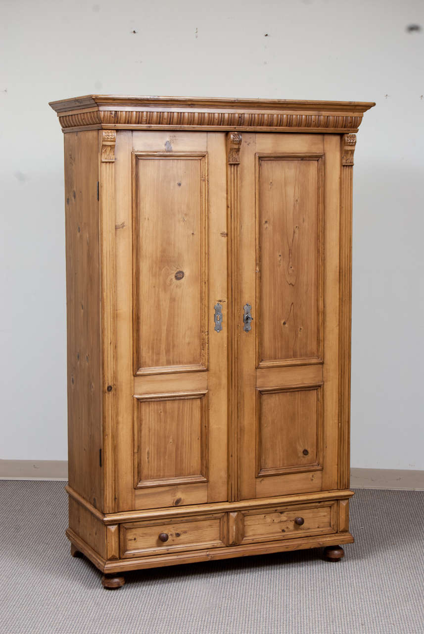 One of a matched pair of small pine armoires featuring two wide-swinging panelled doors beneath a decorative crown molding, flanked and separated by fluted molding and corbels with a single hand-cut dovetailed drawer.
