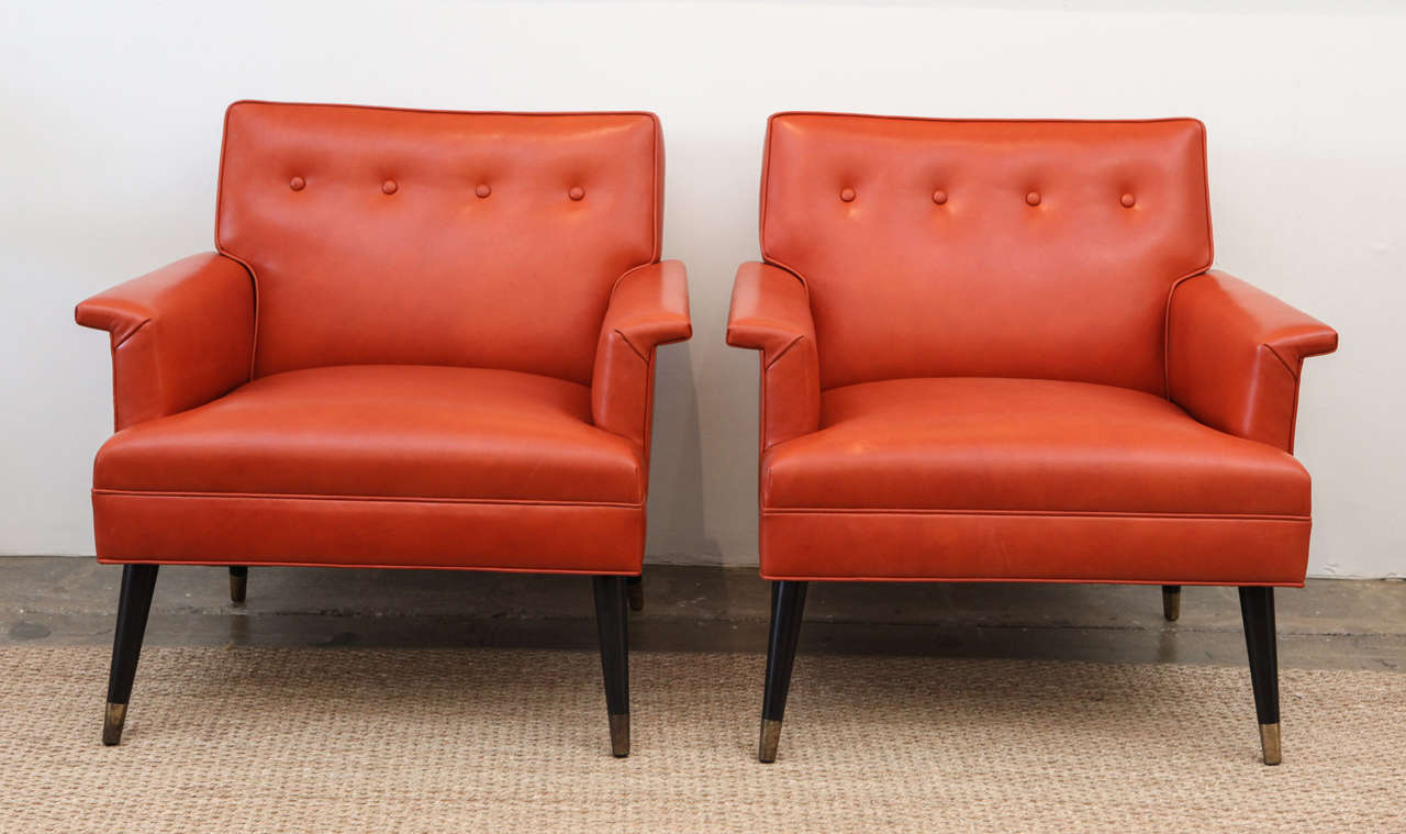 These beauties have been reupholstered here in Los Angeles with a beautiful orange leather and feature their original brass feet on black tapered legs. With four buttons across the back and unobtrusive arms, these chairs are incredibly comfortable