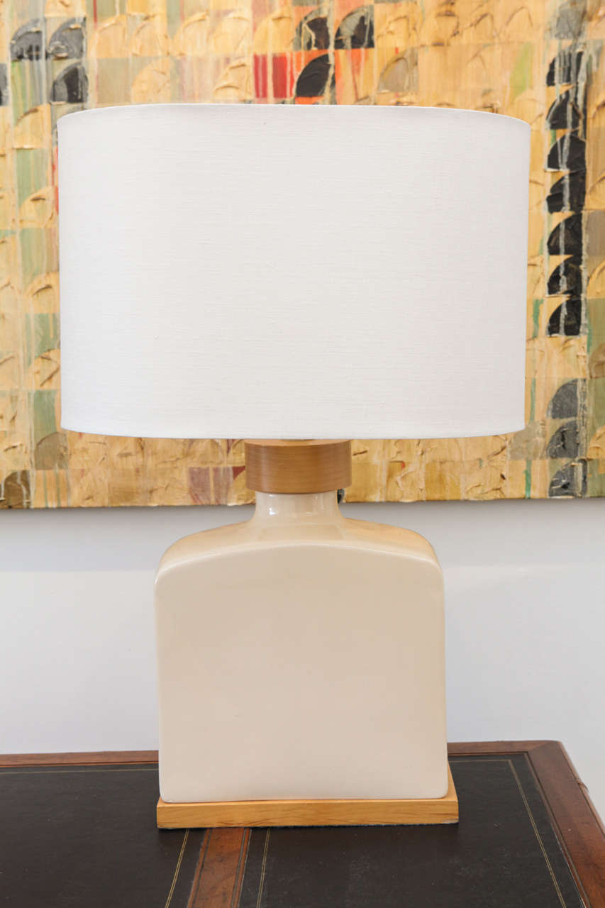 This pair of creamy, off-white ceramic lamps have a birchwood base, as well as a wider birch detail encircling the lamp's neck. The white linen oval shades are new and measure 18