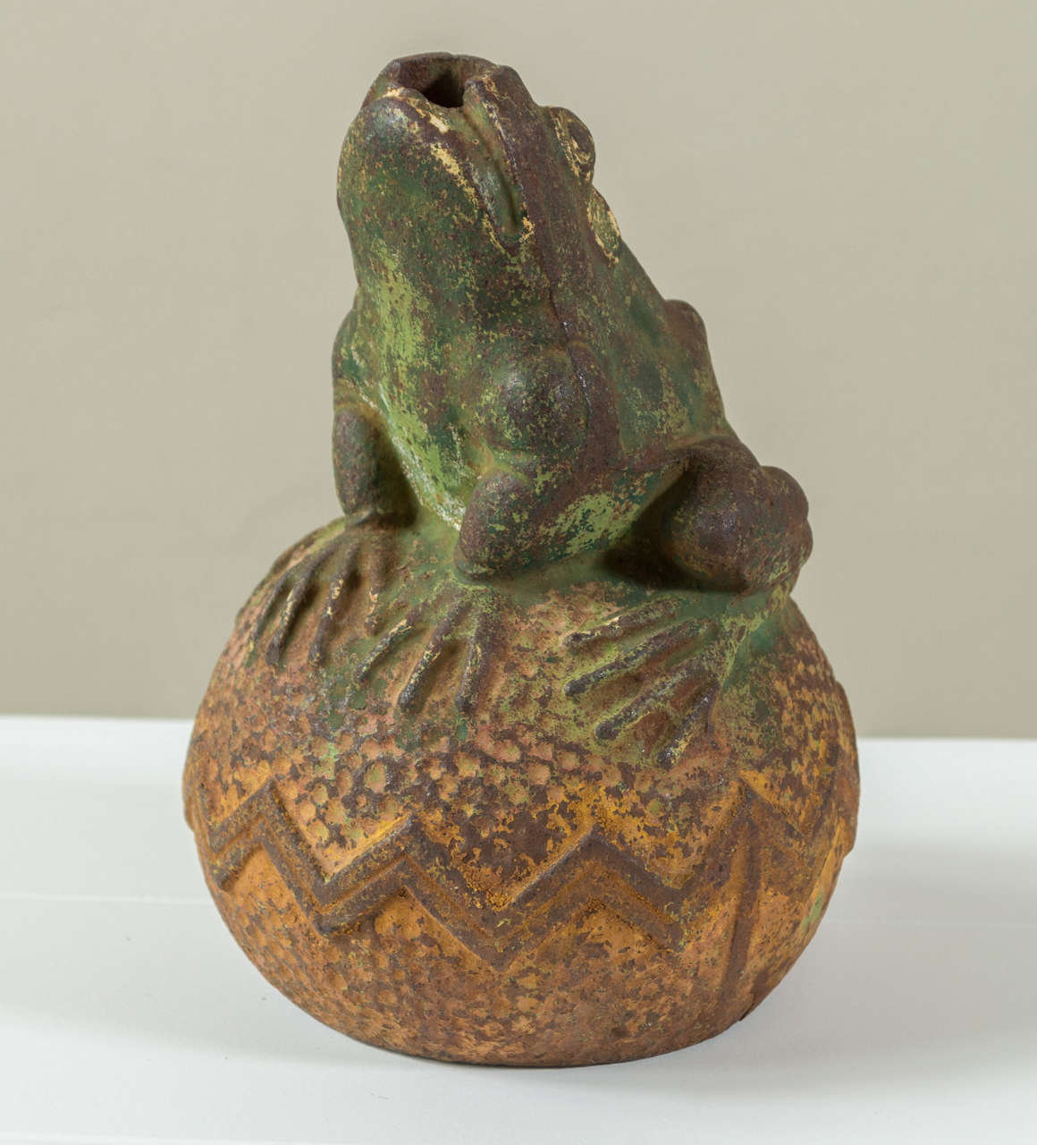 A rare early 20th century cast iron fountain head in the form of a frog on zig zag decorated ball retaining traces of polychrome finish