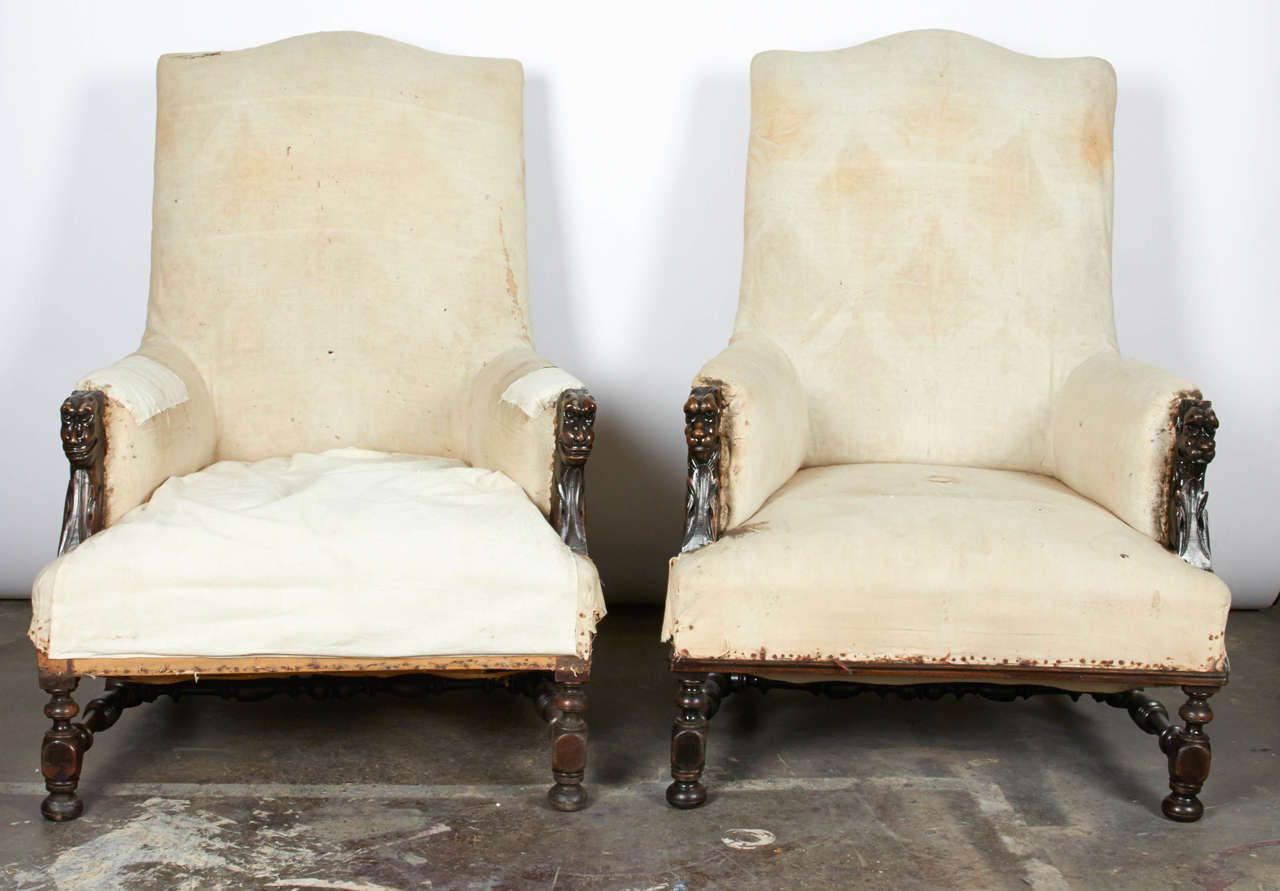 Ornate yet masculine pair of carved walnut armchairs awaiting your final decorative touch. Chairs come as-is with exposed burlap lining on the sides and muslin elsewhere. Turned stretcher and legs are sturdy. Carving of a beast's face completes the