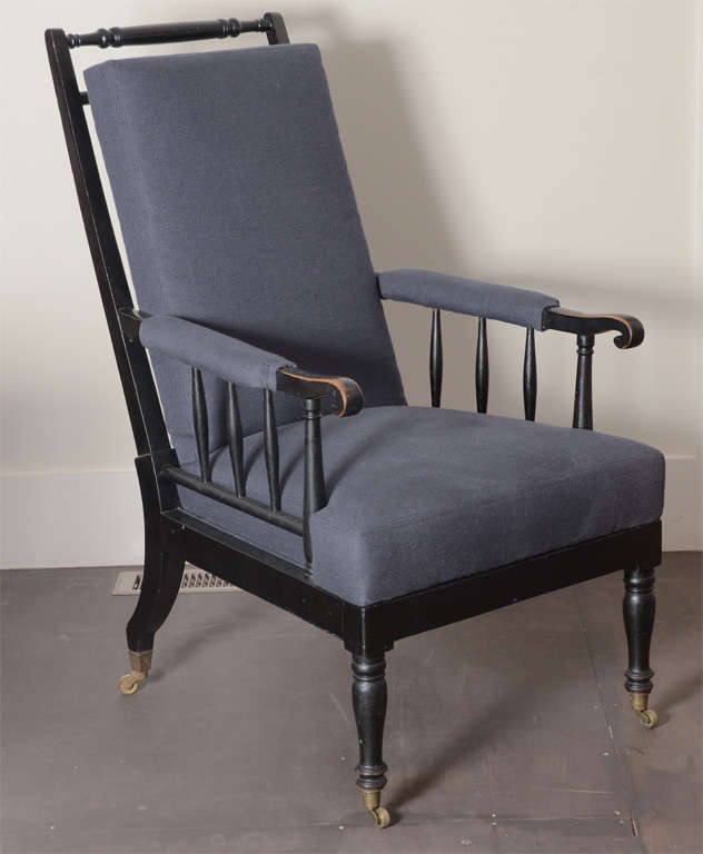 Antique William Morris painted black arm chair with classic spindle arms and back, turned legs, brass casters. Beautiful antique patina on arms. Newly upholstered in navy blue linen. Seat Height: 17.5