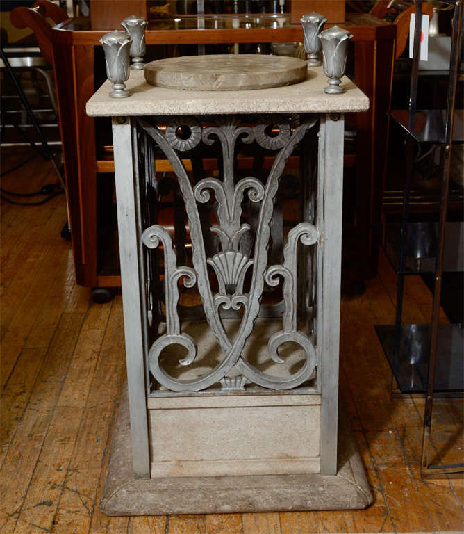 A Art Deco pedestal in marble and limestone by Edgar Brandt for Ferrobrandt. The piece has cast aluminum detailing of scrolling vine and floral detail on the sides with flower bulb finials.
