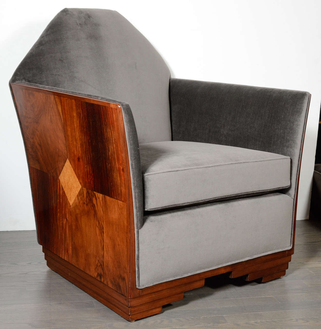 This stunning Art Deco Skyscraper style chair features book matched inlaid burled walnut & elm in a Art Deco geometric design. It has fine, splayed arms, an upholstered apron with a stepped skyscraper style base. Upholstered in luxurious platinum