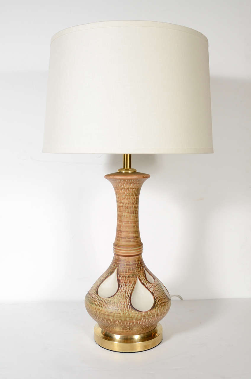 These hand-painted ceramic lamps were realized in the United States, circa 1960. They feature sculptural and sinuously curved forms with inset tear drop patterns in a bone hue; brushed brass circular bases; and a beautifully mottled tawny brown