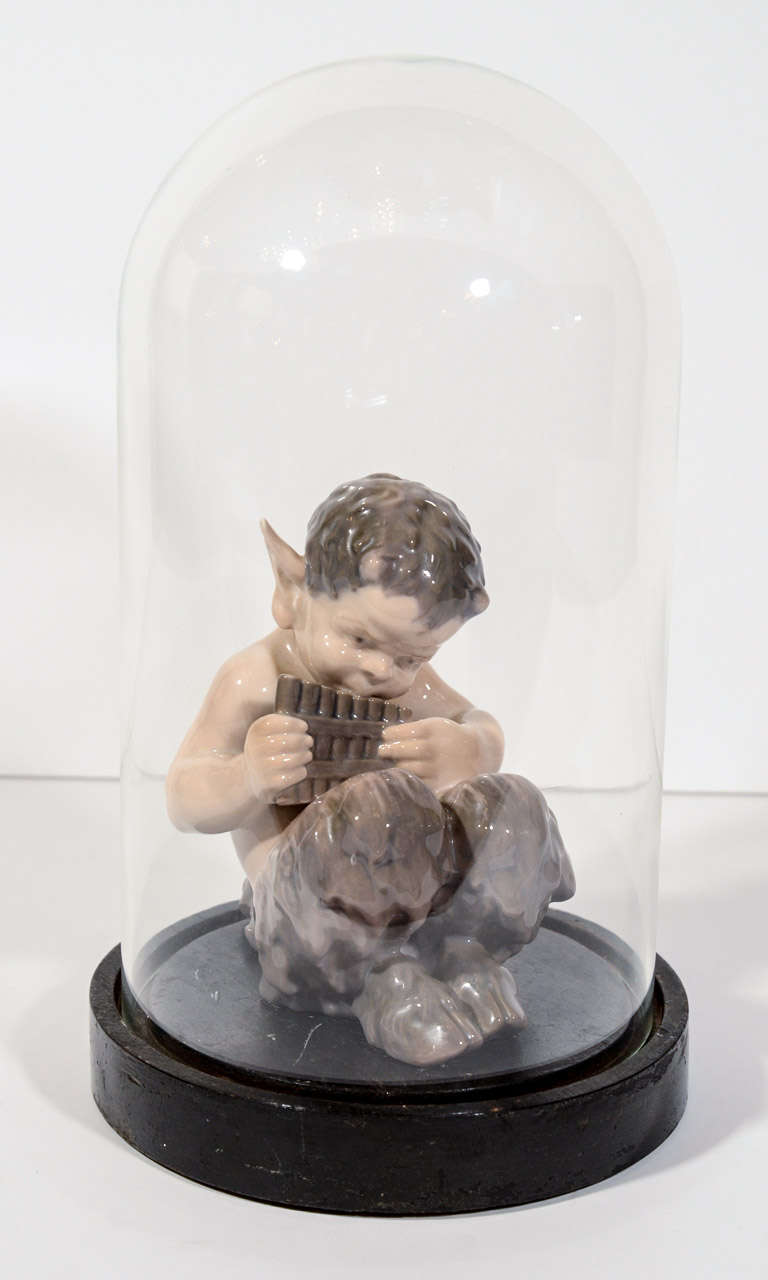 Rare hand made porcelain figurine of faun or satyr playing pipes. Shown in an antique Victorian display dome with glass top and hand carved circular wooden base.  Signed Royal Copenhagen OHX and numbered 1736.