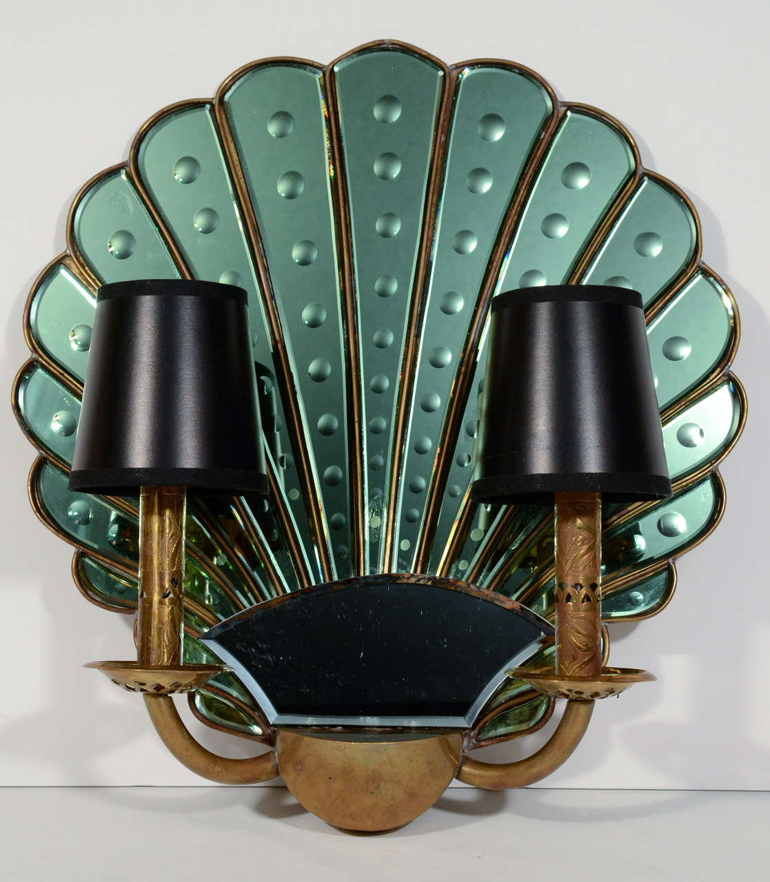 Pair of highly stylized Art Deco sconces.  The sconces are comprised of large scalloped backplates with shell or fan design in emerald green tinted mirror. The mirrored insets have reverse etched convex circle designs. The sconces have a darkened