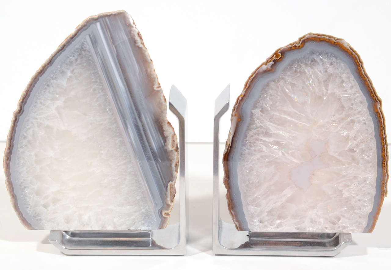 Pair of elegant hand cut polished and raw agate stone bookends with crystalized quartz centers.  The bookends have hues of variant grey and neutral colors along the inside borders, with raw outer edges. Fitted with modernist polished chrome stands.