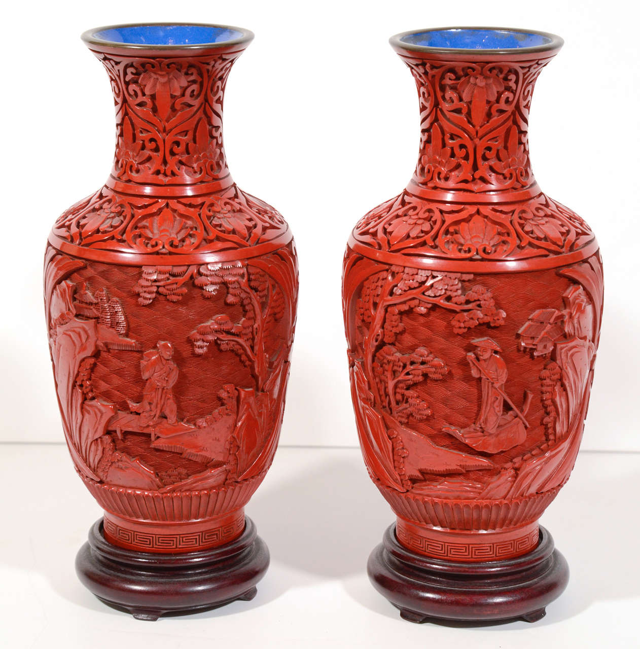 Pair of fine hand made Chinese porcelain vases with red lacquered (cinnabar) exteriors. The vases feature carefully hand crafted Asian sceneries and motifs and have blue glazed interiors with bronze trimmed borders. Also includes hand carved wooden