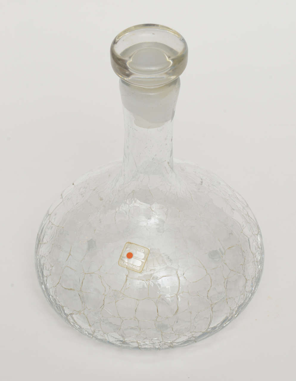 The crackled glass of this vintage Blenko decanter with it's original glass stopper has the original and vintage plastic label on the glass. The bulbous form and shape is wonderful with the crackled glass effect. It is very modernist and timeless!