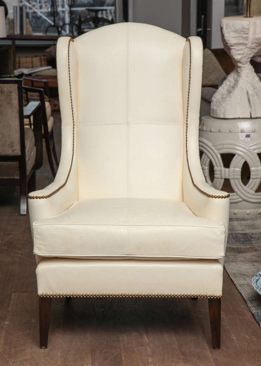 Pair of dramatic high wingback chairs with flat scrolls arms circa 1950 reupholstered in glazed ivory leather with saddle stitching, French natural nailheads and contrast French twill outside back and sides
