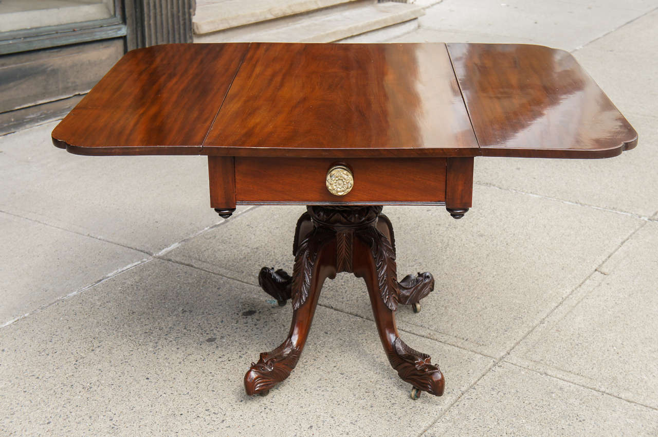 This finely made American drop-leaf library or breakfast table was made in Glens Falls New York before 1835. The extensively and deeply carved pedestal base resting on extended eagle head carved feet show the cabinet makers hallmark feature resting