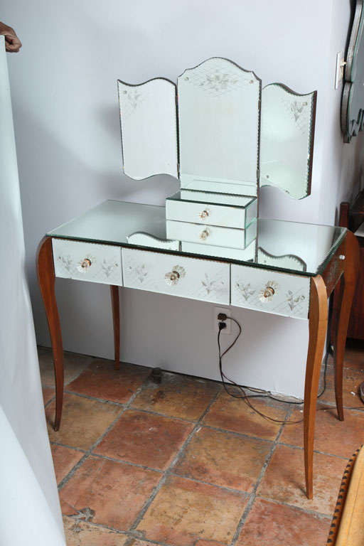 An elegant etched french bevelled mirrored vanity with a  trifold mirror and jewel box The three etched draws have molded glass handles and sits on serpentine fruitwood legs.