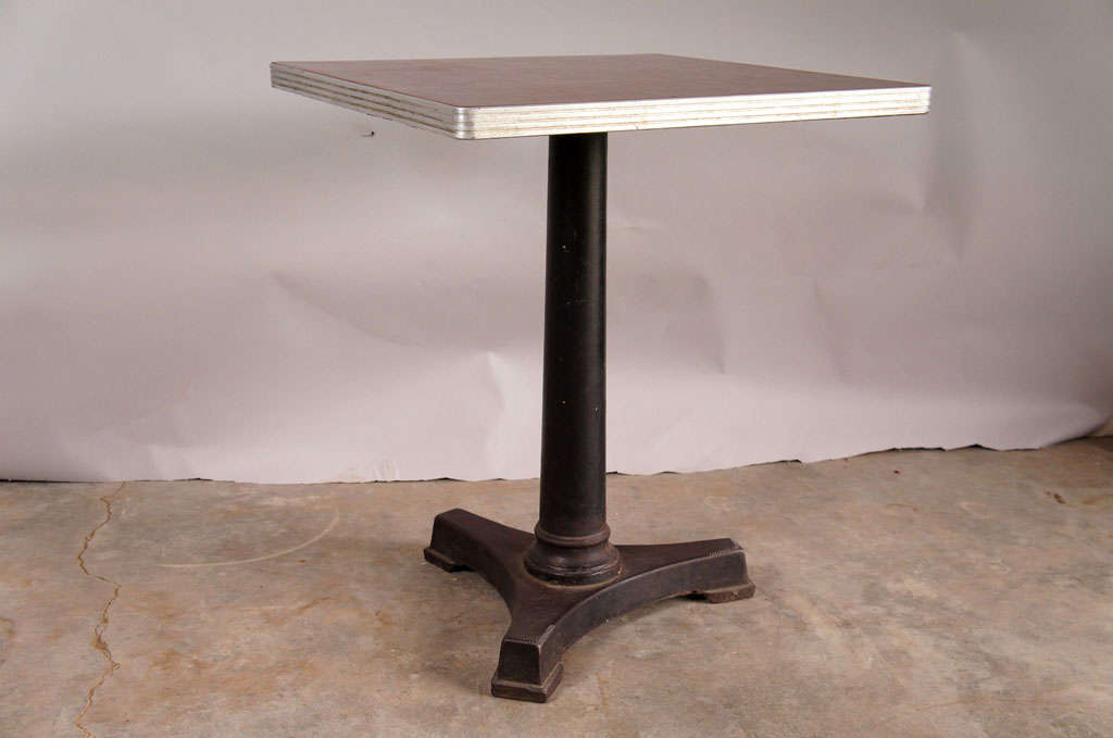 Single cafe table with cast iron base and resin top. Cast iron base with central pedestal and tripod legs. Deep red patterned resin top has aluminium border.
