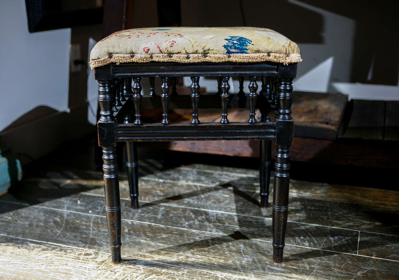 An ebonized stool with spindle apron, ring-turned legs and tapestry upholstered seat