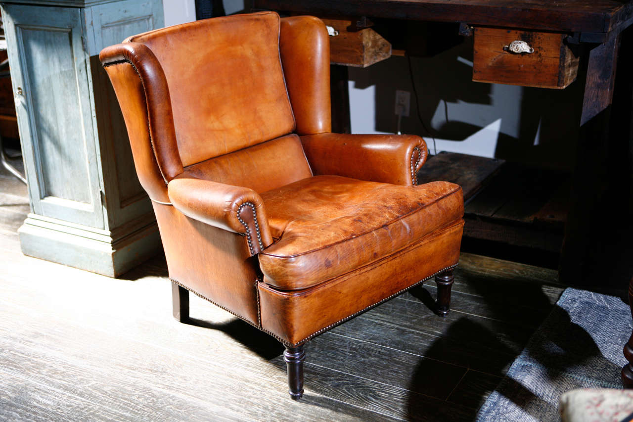 A wing chair in camel colored leather with stud trim and ring-turned legs