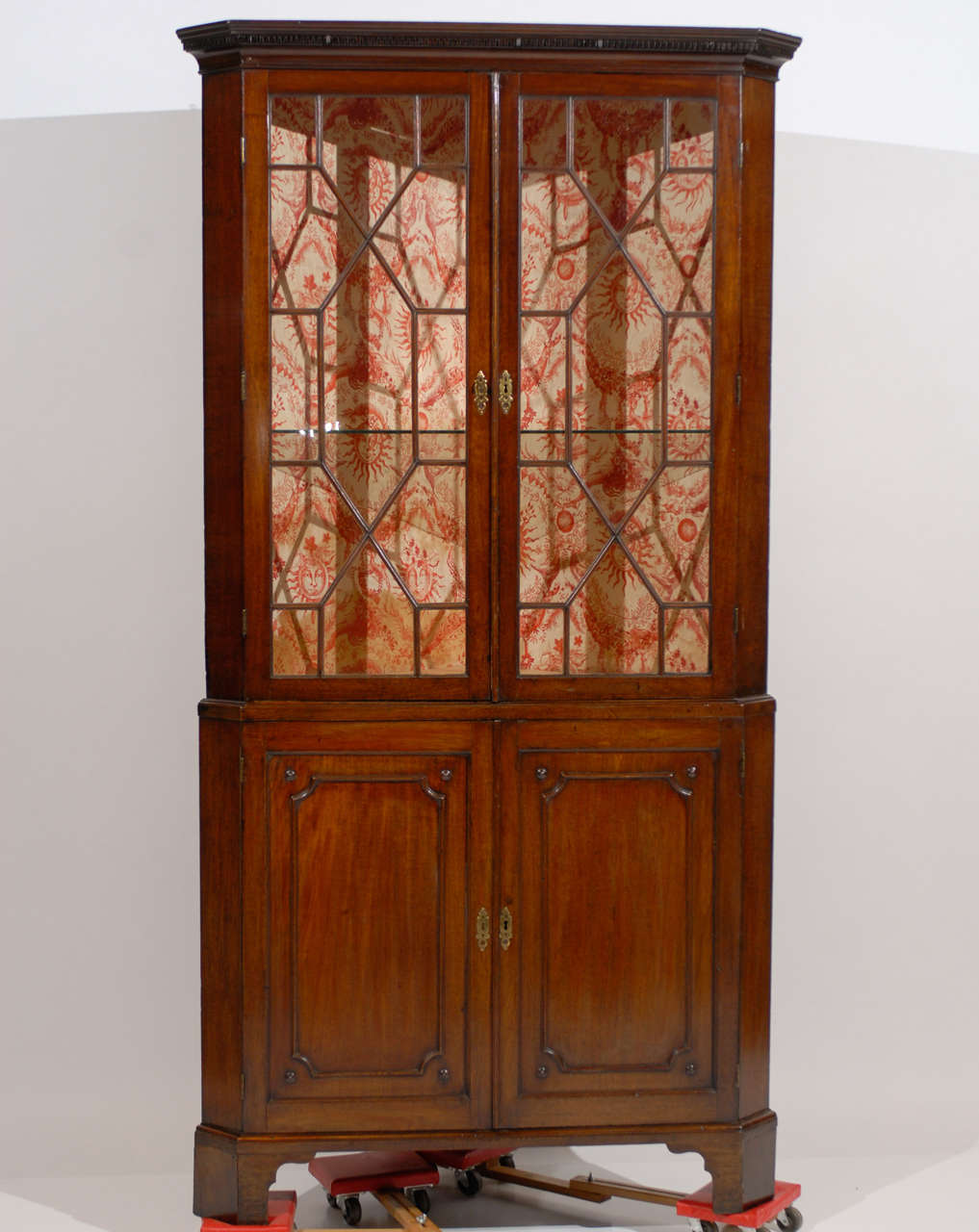 A George III carved mahogany corner cabinet with dentil molded canted cornice above a pair of 13-pane doors, on lower part having cabinet doors with applied molding with interior shelving. All resting on bracket feet. 

William Word Fine Antiques: