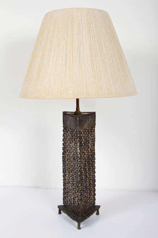 A Brutalist table lamp in a triangular column form comprising perforated steel planes and a triangular metal base with three metal feet. After Paul Evans. U.S.A., circa 1970.