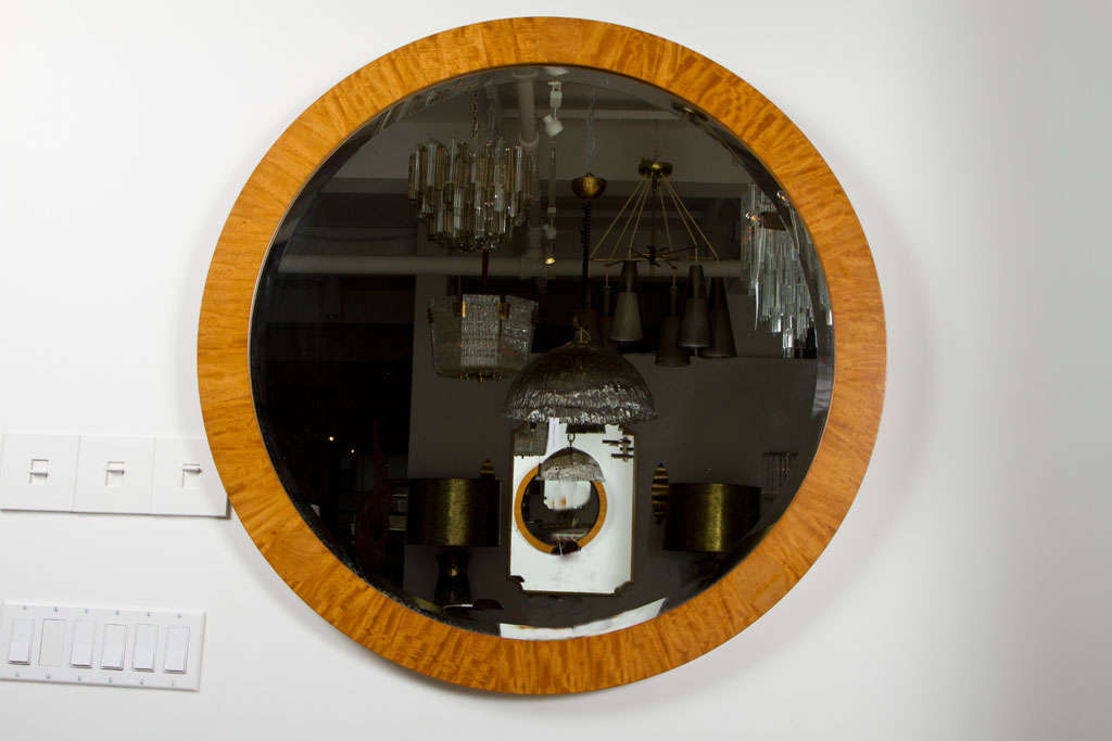 An elegant mirror in a circular form with honey colored veneers of ribboned prima vera (white mahogany), circular parquetry inlays (one at the top and two at the bottom) and a beveled circular mirror. Retains original makers label to the back side.