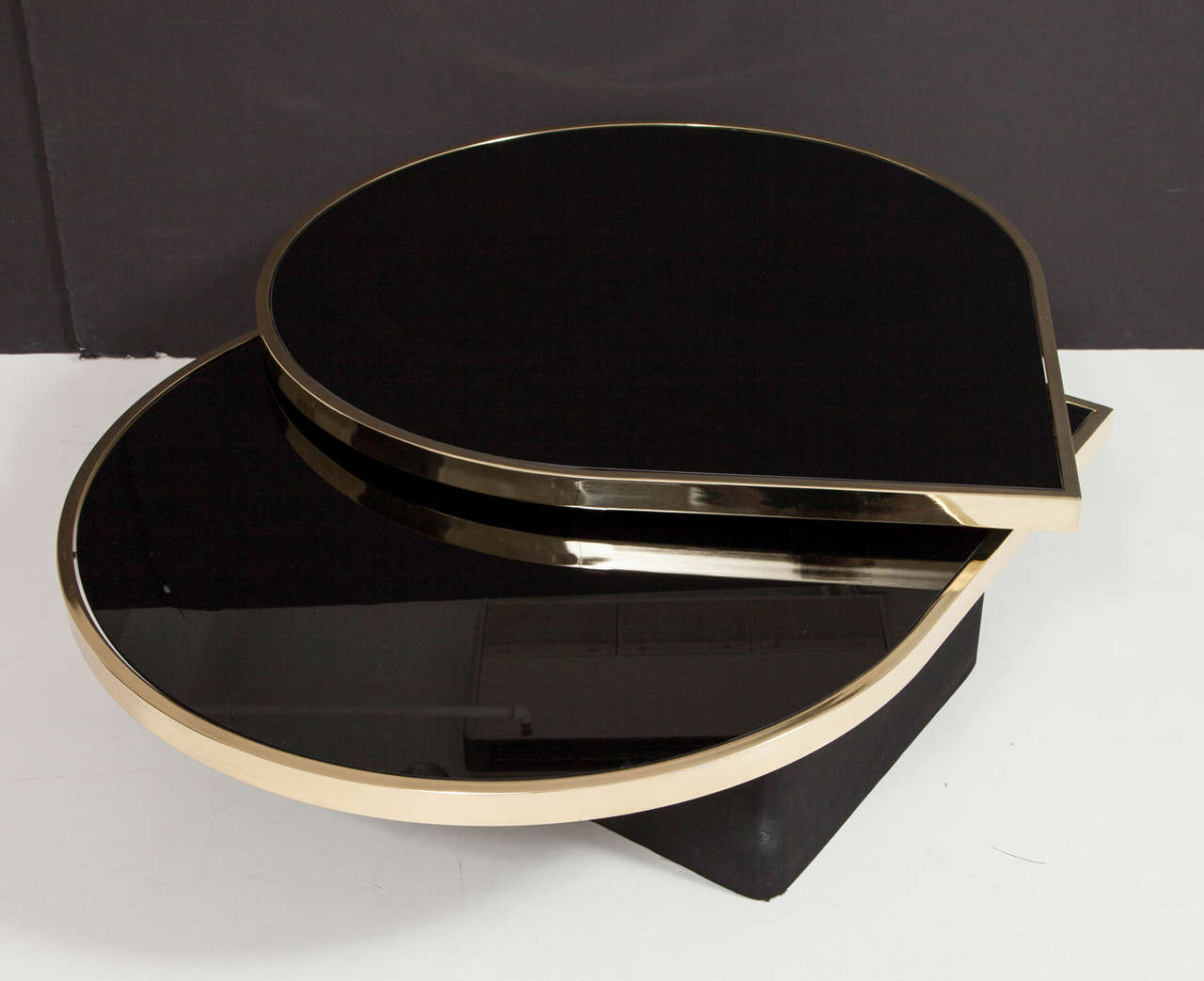 Elegant reverse black painted glass and polished brass cocktail or coffee table floating on a black suede covered base designed and manufactured by Design Institute of America (DIA). The top rings swivel or rotate out to form multiple