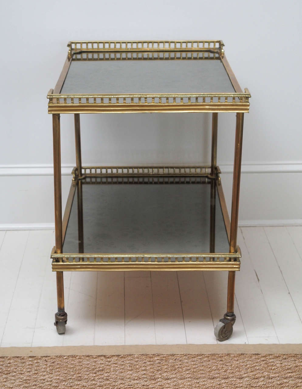 French vintage bar cart in solid brass and glass with finely cast galleries and original mirrored black glass shelves, on casters. A very elegant and heavy piece with flawless cast details and a warm patina. This piece would be perfect as a bar cart