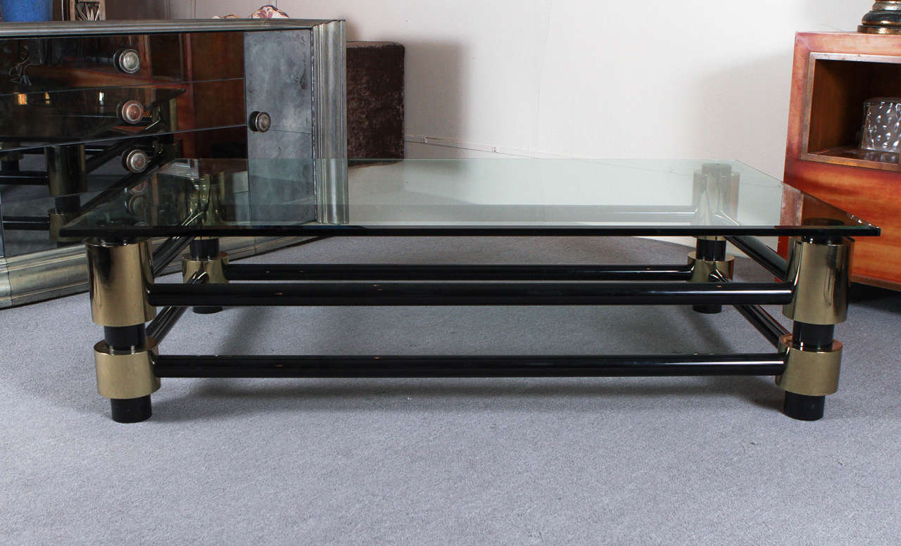 Impressive coffee table by Ron Seff. The 3/4 inch beveled glass top sits upon a beefy base with cylindrical brass legs that are connected with metal tubes which have a beautiful black enameled finish.