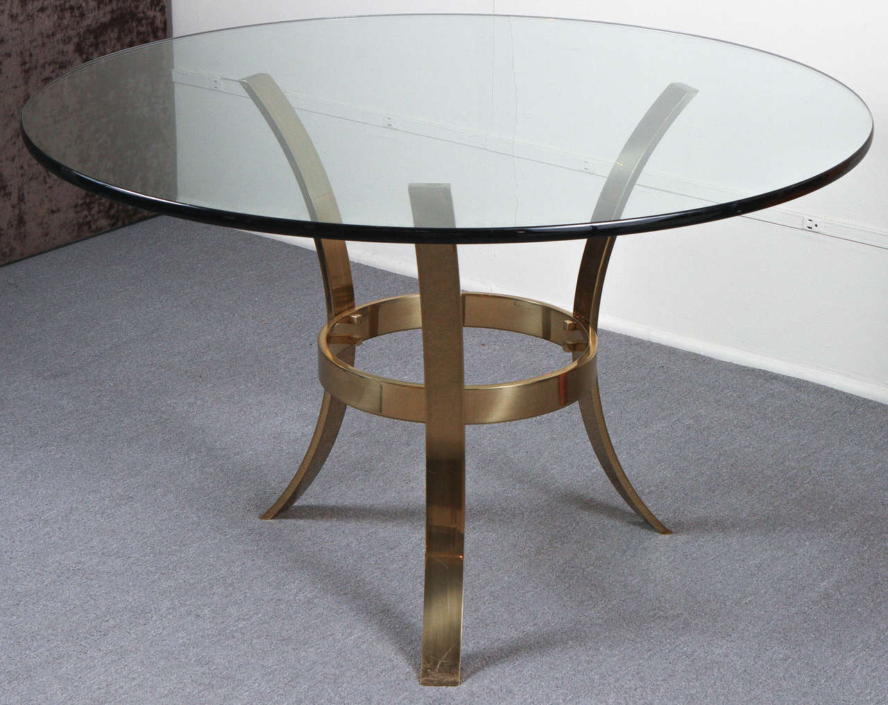 Large entry table with a beefy tripod base of polished brass and a circular glass top.
The base is detailed with bolts that have cubed heads.